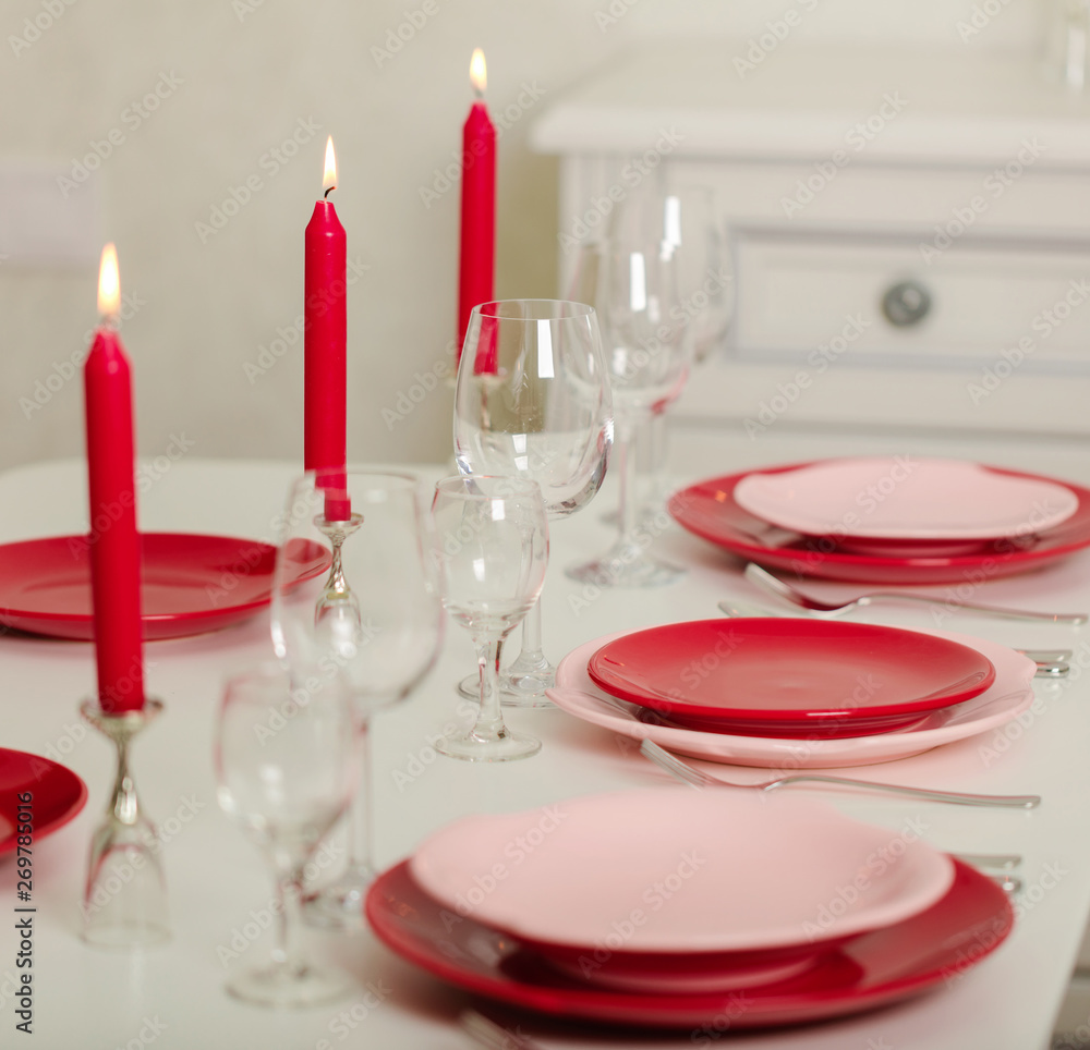Merry Christmas and Happy New Year! Table setting - red and pink dishes, holiday knitted decor - Santa Claus knitted hats on the bottle with wine, red candles. Merry Christmas and Happy New Year! Table setting - red and pink dishes, holiday knitted decor - Santa Claus knitted hats on the bottle with wine, red candles.