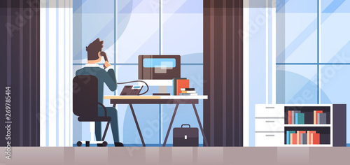 businessman sitting at workplace desk rear view business man using computer while talking on landline phone working process concept creative office interior flat horizontal