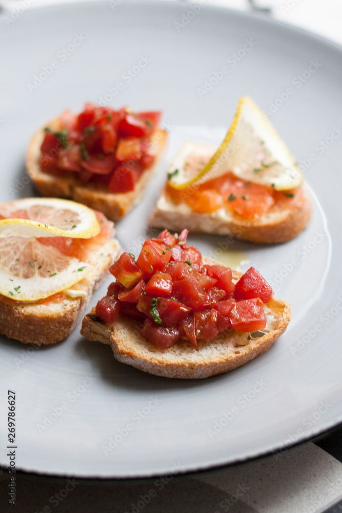 A plate of croutons with salmon and vegetables decorated with lemon slices.