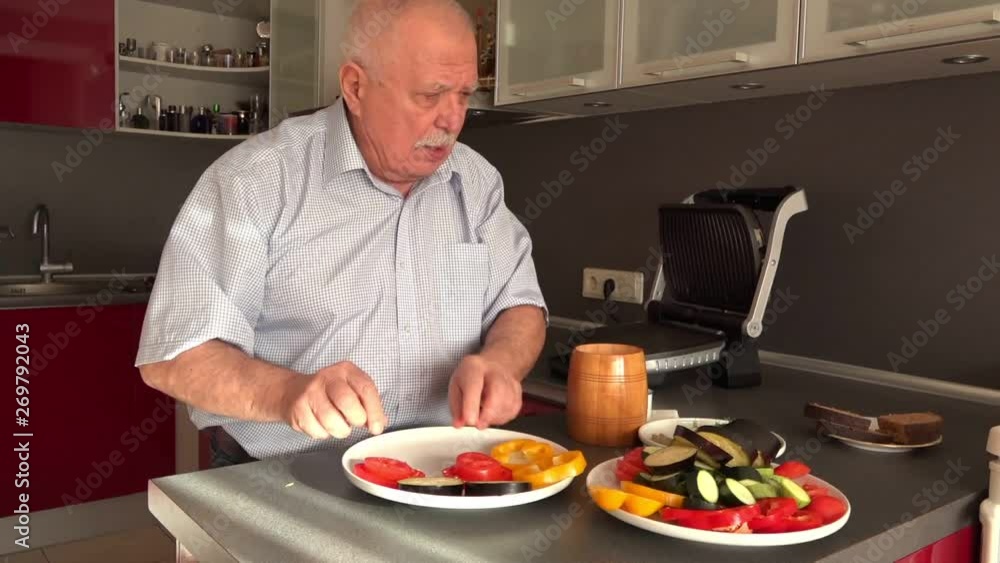 senior man takes zucchini from big plate with cut vegetables and puts onto yellow bell pepper slice close view senior man takes zucchini from big plate with cut vegetables and puts onto yellow bell pepper slice close view