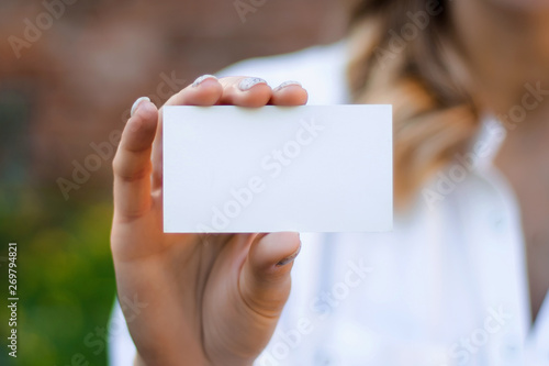 Women's hands holds a business card a mock up for the presentation of the design. Female hand holding a white business card with copy space on a a brick wall background