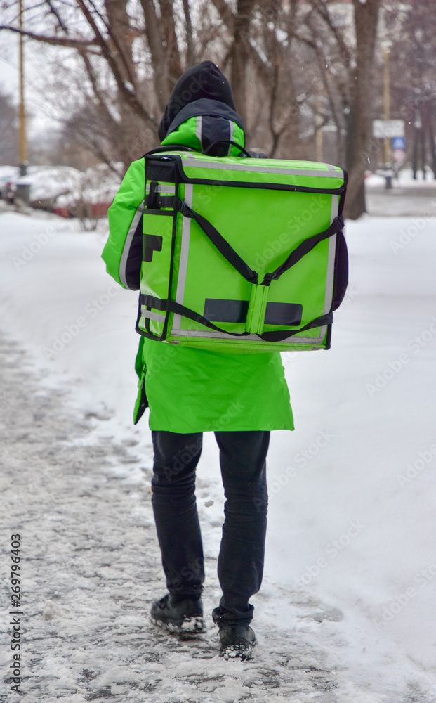The delivery man is walking down the street. He is wearing green overalls and a special rectangular transport backpack. Mock up blank for text and advertising