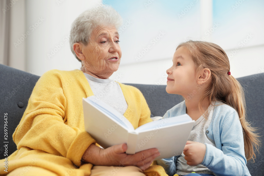 Fototapeta premium Cute girl and her grandmother reading book at home