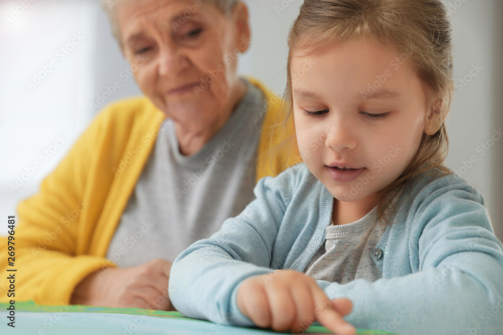 Cute girl and her grandmother reading book at home Cute girl and her grandmother reading book at home