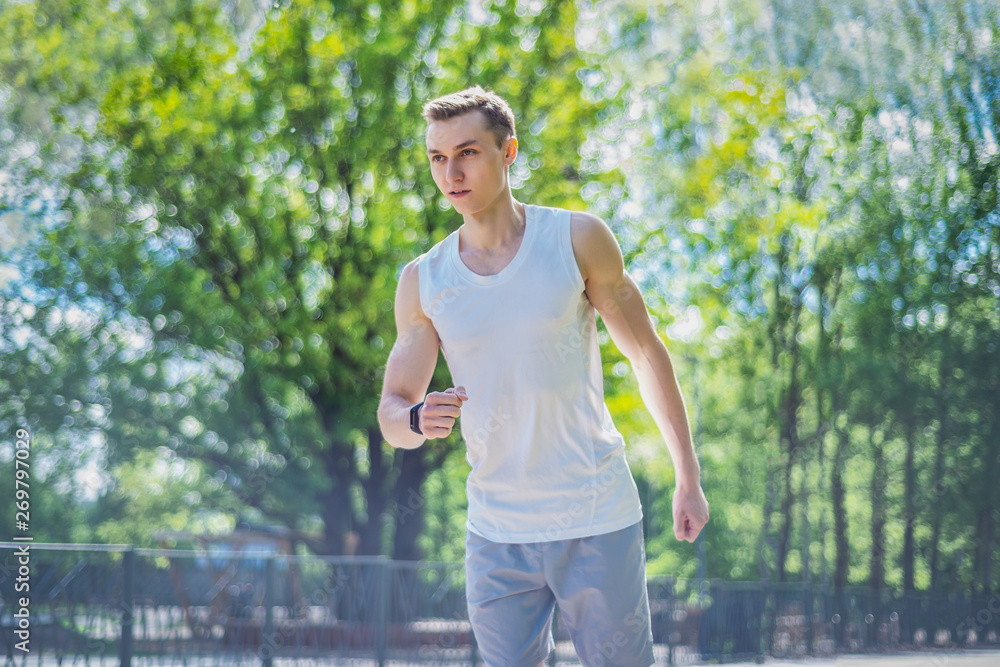Young sporty man runs on a sunny day in the park. He wears sportswear and fitness tracker