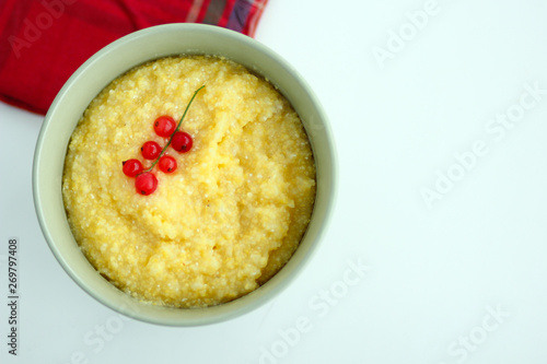 View from above of maize porridge in bowl with branch red currant on it served with red napkin on white table
