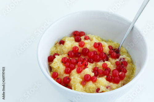 Photos Homemade healthy maize porridge with red currant in white bowl on the white tabl