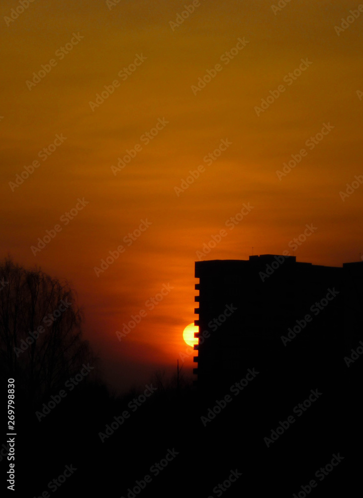 The black silhouette of the house against the bright orange sunset. The sun is setting beautifully. The view of the sunset.