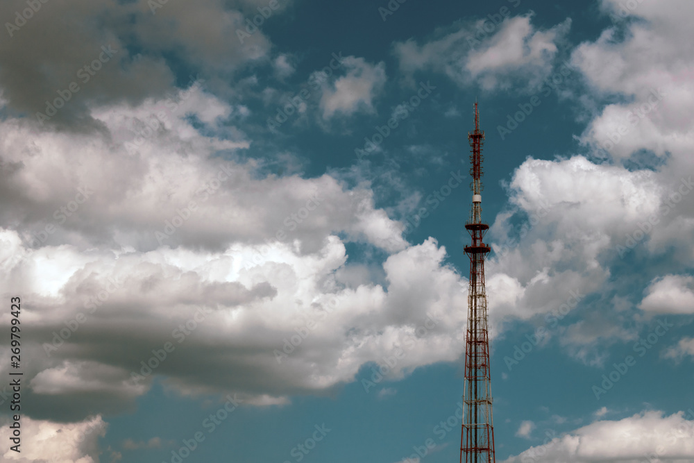 Radio tower antenna on a background of blue sky with white clouds. Telecommunication transmitter global telephone equipment Radio tower antenna on a background of blue sky with white clouds. Telecommunication transmitter global telephone equipment
