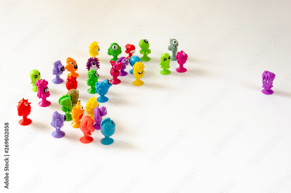 A single character faces a group of figures. Colorful rubber monster figurines on white background. Concept of the conflict between a single and a group A single character faces a group of figures. Colorful rubber monster figurines on white background. Concept of the conflict between a single and a group