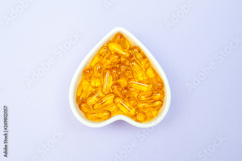 Heart-shape plate with fish oil capsules omega 3, healthy product and supplement concept close up, flat lay