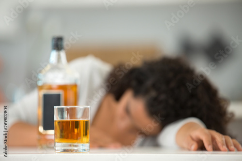woman slumped over beside a bottle of alcohol