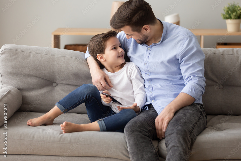 Happy dad and preschooler son relax on couch together Happy dad and preschooler son relax on couch together