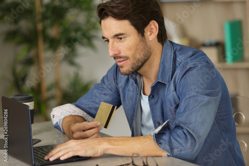 man using laptop and holding bankcard