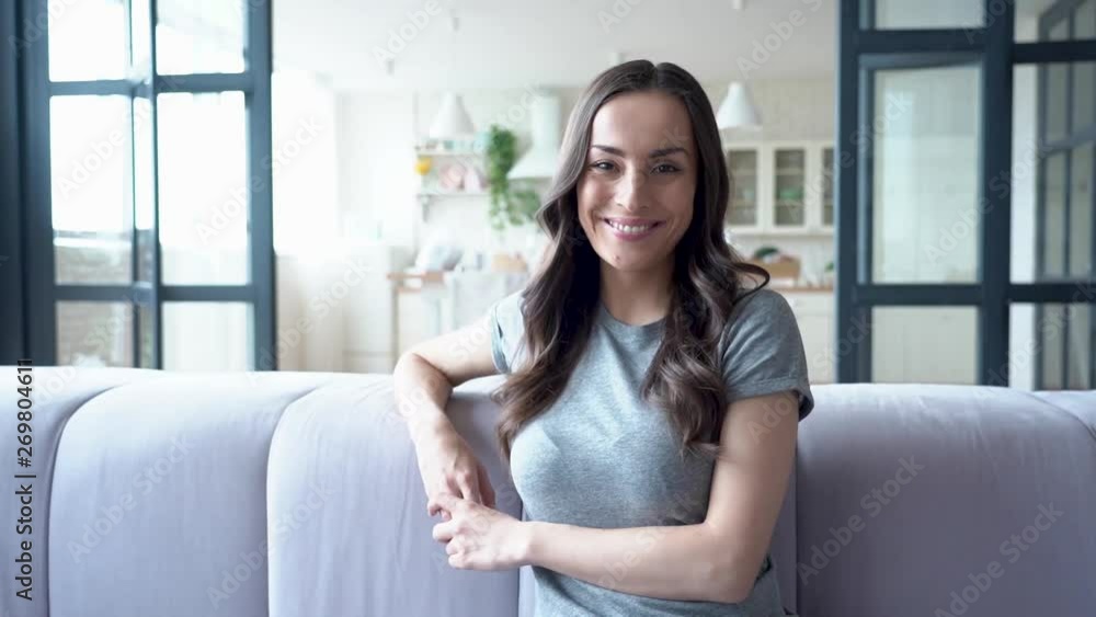 Relax and concentrate at home. Portrait of smiling cute lovely brunette woman in casual clothes while she sitting on sofa at home and looks on camera. Relax and concentrate at home. Portrait of smiling cute lovely brunette woman in casual clothes while she sitting on sofa at home and looks on camera.