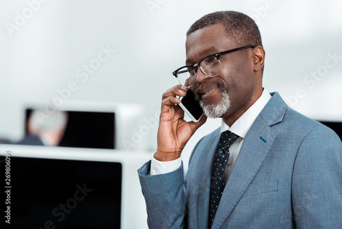 handsome african american businessman in suit talking on smartphone in office