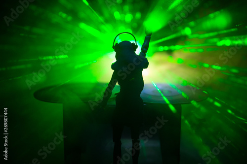 Dj club concept. Woman DJ mixing, and Scratching in a Night Club. Girl silhouette on dj's deck, strobe lights and fog on background. Creative artwork decoration with toy.