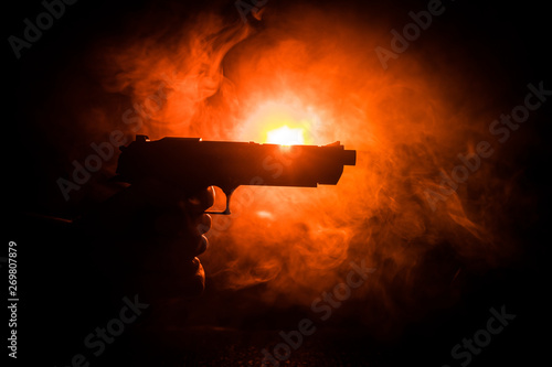 Foto Male hand holding gun on black background with smoke toned back lights