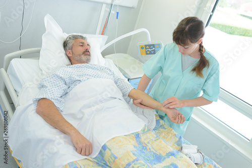 nurse taking pulse of patient in hospital bed