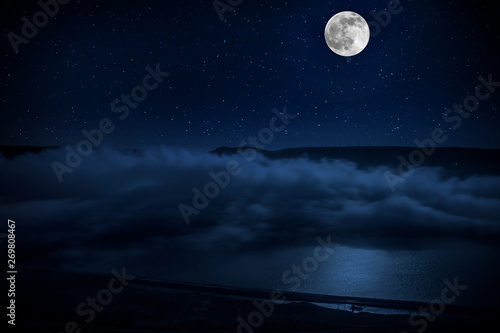Photo This dramatic moon rise in a deep blue night time sky is accented by highlighted clouds and beautiful, calm lake reflection