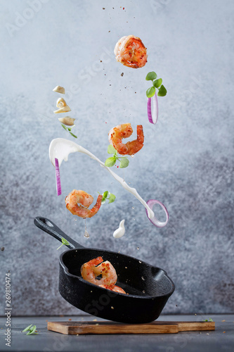 Fresh fried shrimp fly into a pan. Sea food with garlic, onion, cream, spices and basil flying into a pan on modern concrete background. Food preparation, meal ready for cooking.