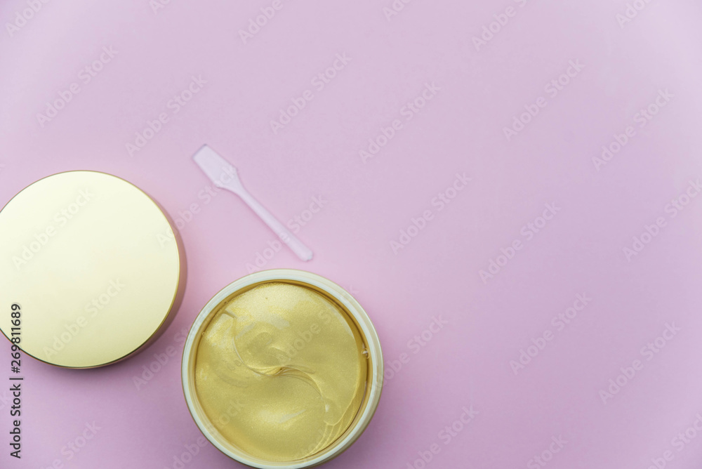 Hydrogel cosmetic eye patch jar with golden patches against dark circles under eyes with spoon. Beauty health care concept. Flat lay set on pink background. 