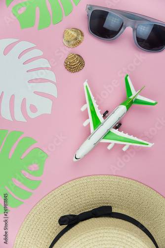 Flat lay traveler accessories on trendy pink background with straw hat, palm leaf, airplane, sea shells and sunglasses. Top view travel and planning summer vacation concept. 