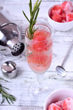 Sparkling cocktail with watermelon balls and rosemary in a champagne glass on white table