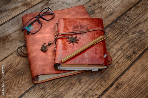 Vintage writing materials still life: two brown leather vintage notebooks or books, glasses and vintage metall brass pen on old antique wooden table or floor. HDR image