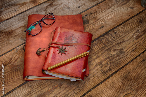 Foto Vintage writing materials still life: two brown leather vintage notebooks or books, glasses and vintage metall brass pen on old antique wooden table or floor