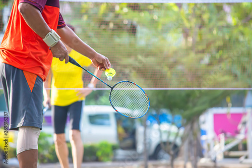 Elderly man Hand holding a badminton racket Background blur tree in park. © Nueng