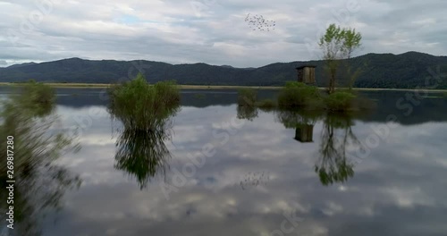 Flying low over the Cerknisko lake in Slovenia with amazing reflections and hunter post in the background 4K photo