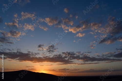 Orange sun during sunset with reflexion through clouds as seen from a dune in Dunhuang, Gansu province, China. 