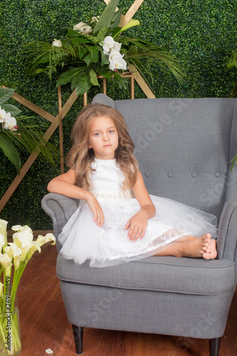 Little cute girlswith blond hair in a white dress and white flowers, lilies and orchids on a green background photo