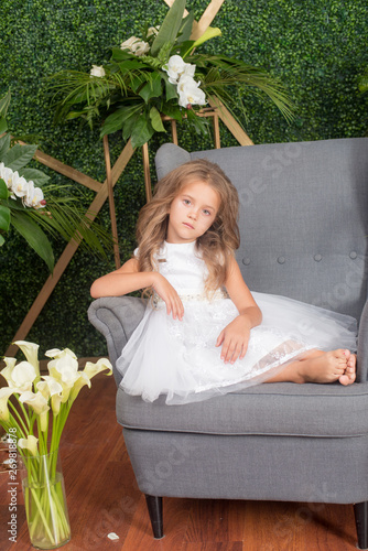 Little cute girlswith blond hair in a white dress and white flowers, lilies and orchids on a green background photo