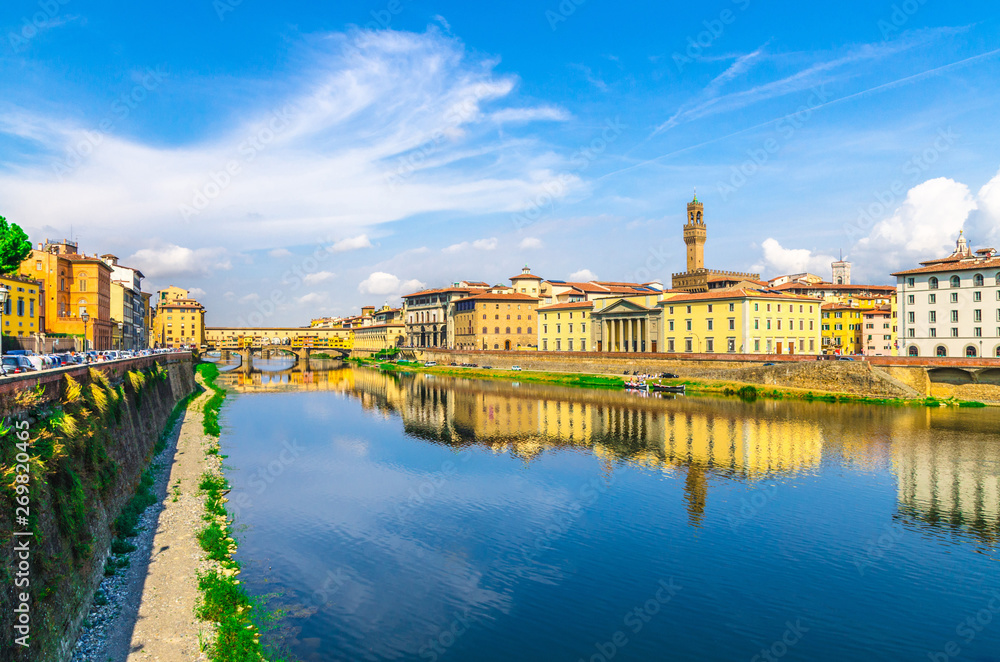 Ponte Vecchio bridge with colourful buildings houses over Arno River blue reflecting water and embankment promenade in historical centre of Florence city, blue sky white clouds, Tuscany, Italy