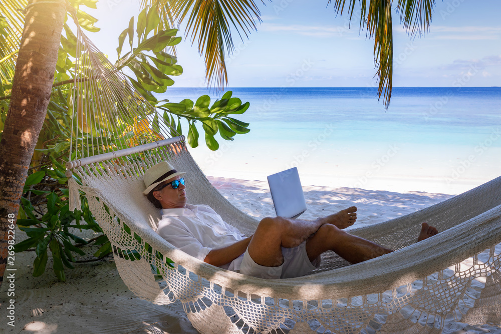 Arbeiten im Urlaub: Mann mit Laptop auf Hängematte am tropischen Strand  unter Palmen Stock Photo | Adobe Stock