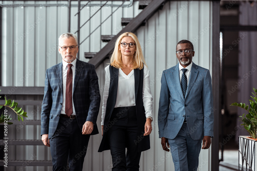 attractive blonde businesswoman walking with handsome multicultural partners in office attractive blonde businesswoman walking with handsome multicultural partners in office