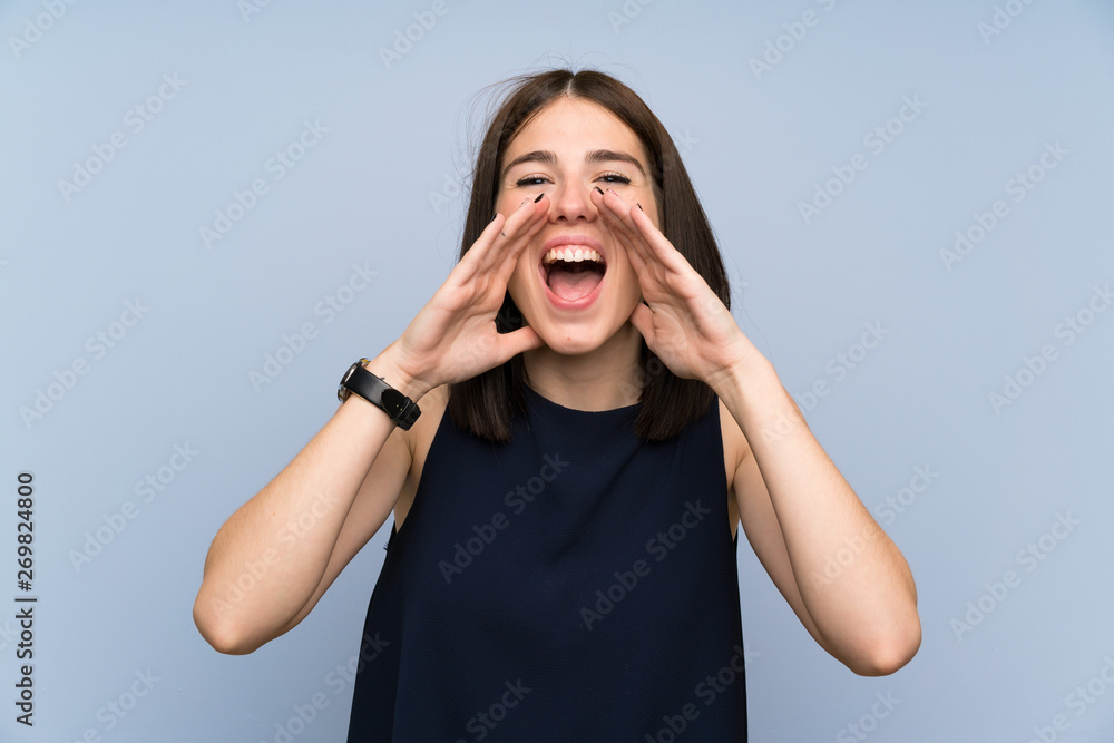 Young woman over isolated blue wall shouting with mouth wide open Young woman over isolated blue wall shouting with mouth wide open