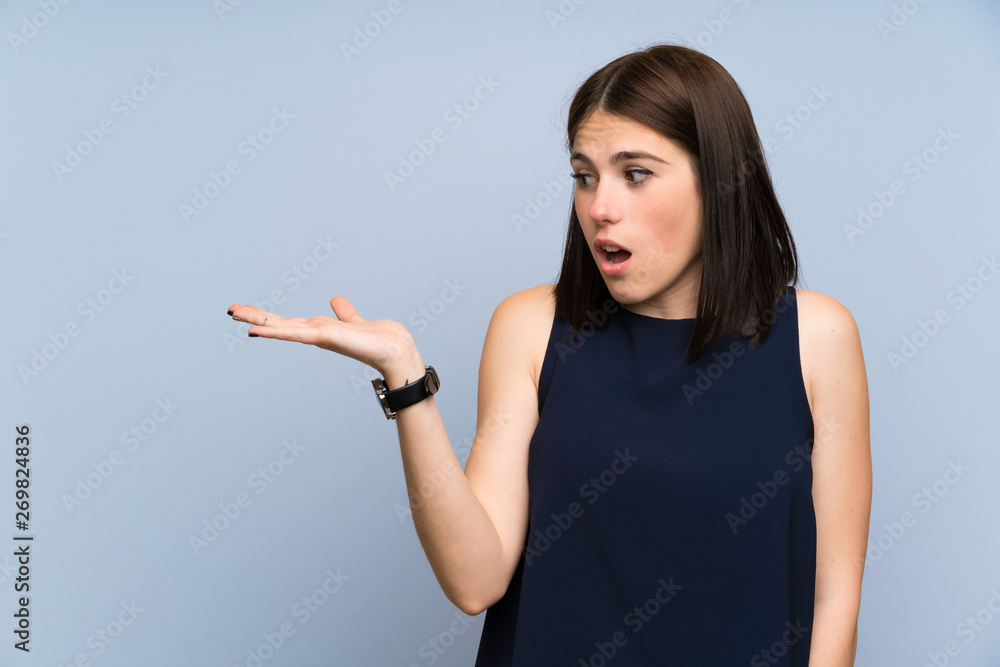 Young woman over isolated blue wall holding copyspace imaginary on the palm Young woman over isolated blue wall holding copyspace imaginary on the palm