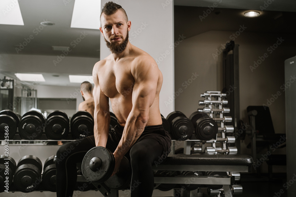 Strong man sitting and lifting dumbbells in the gym Strong man sitting and lifting dumbbells in the gym