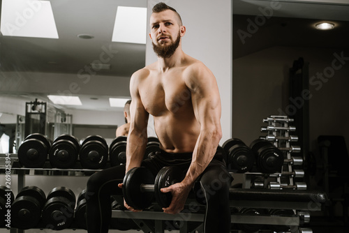 Strong man sitting and lifting dumbbells in the gym