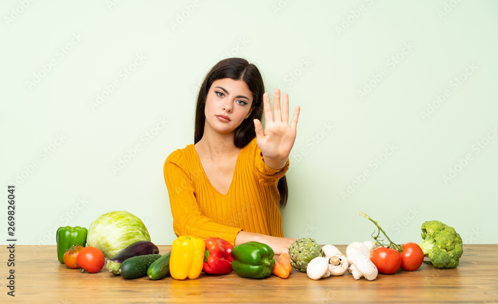 Teenager girl with many vegetables making stop gesture Teenager girl with many vegetables making stop gesture
