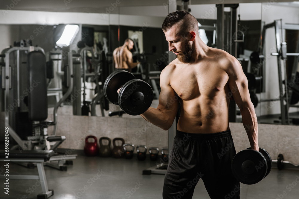 Muscular strong man doing exercises with a dumbbells in the gym Muscular strong man doing exercises with a dumbbells in the gym