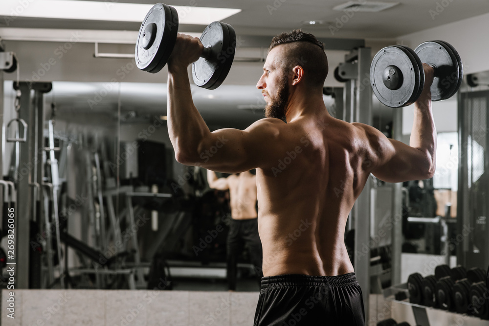 Muscular strong man doing exercises with a dumbbells in the gym Muscular strong man doing exercises with a dumbbells in the gym