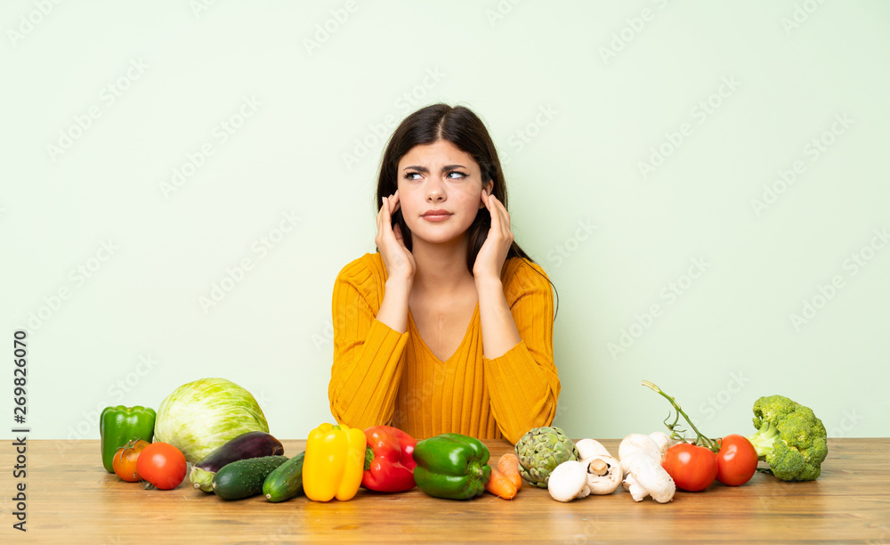 Teenager girl with many vegetables frustrated and covering ears Teenager girl with many vegetables frustrated and covering ears