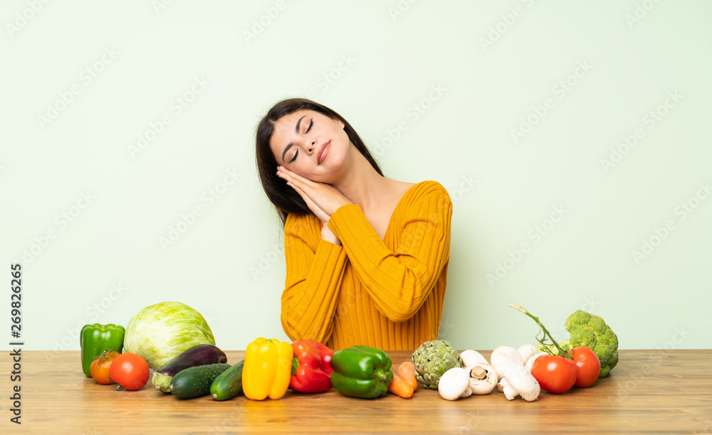 Fototapeta premium Teenager girl with many vegetables making sleep gesture in dorable expression