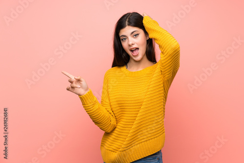 Teenager girl over isolated pink wall surprised and pointing finger to the side