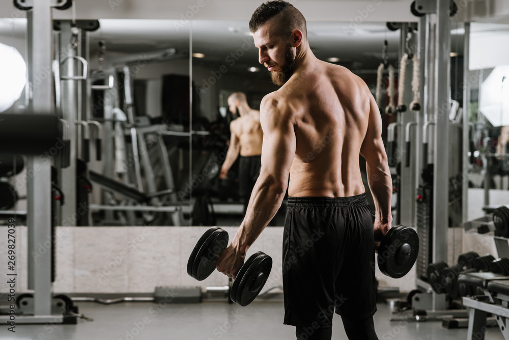 Muscular strong man doing exercises with a dumbbells in the gym