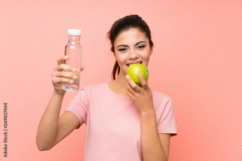 Happy Teenager girl over isolated pink wall with a bottle of water and an apple Happy Teenager girl over isolated pink wall with a bottle of water and an apple